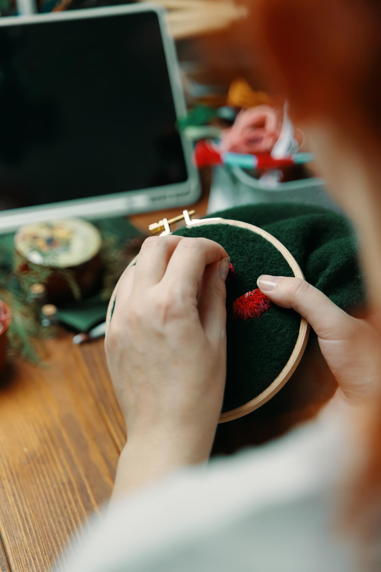 Hands stitching a detailed motif under a lamp